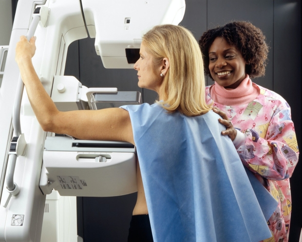 Woman Receives Mammogram. An African-American female technician positions a Caucasian woman at an imaging machine to receive a mammogram. Creator: Rhoda Baer